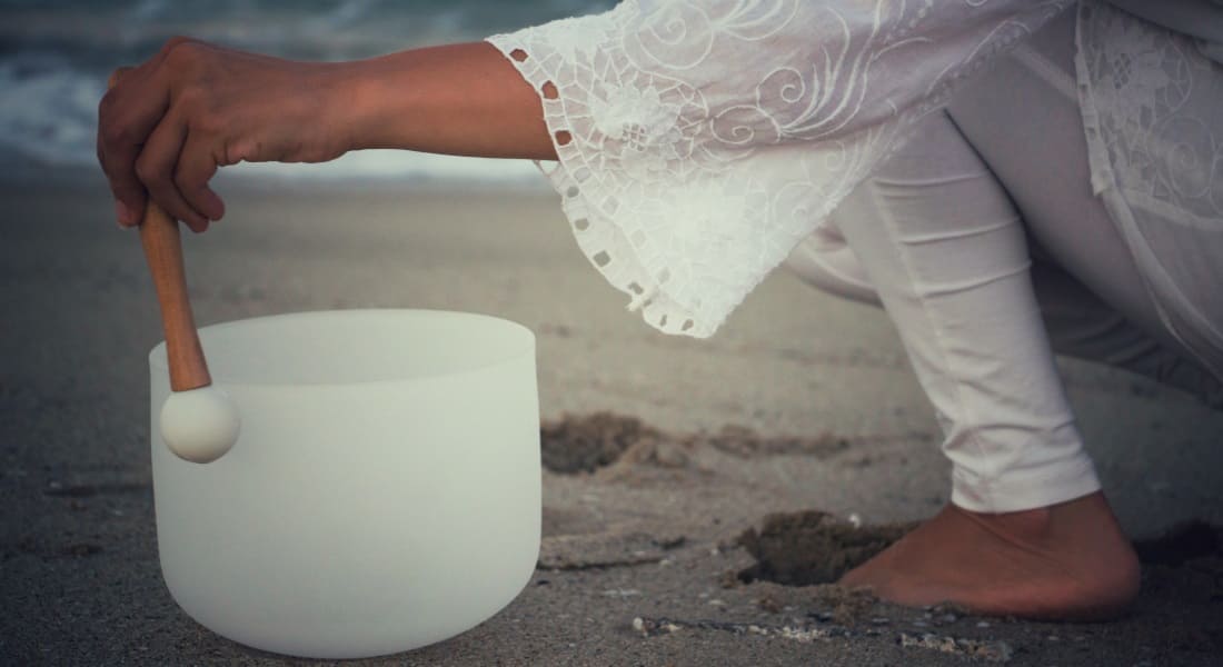 A crystal singing bowl on the sand with someone playing it
