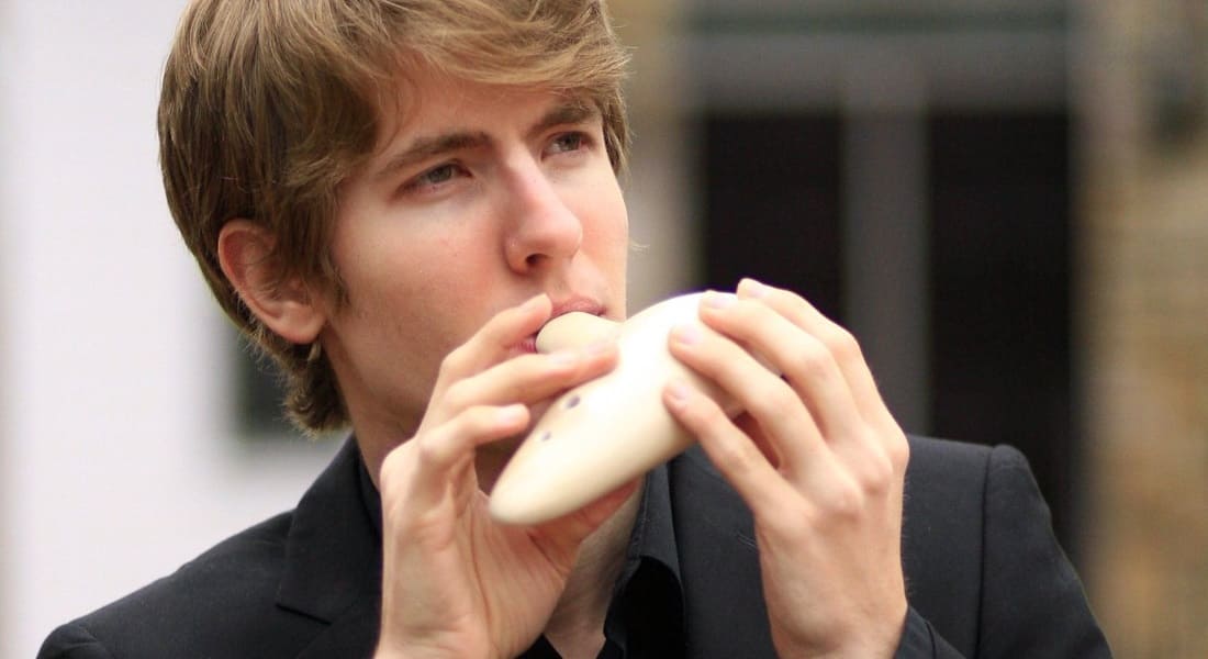 A man playing the ocarina in a black suit