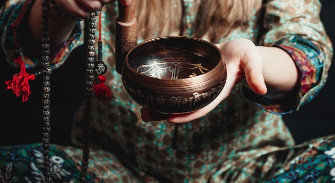 A person holding a singing bowl and a Tibetan mala