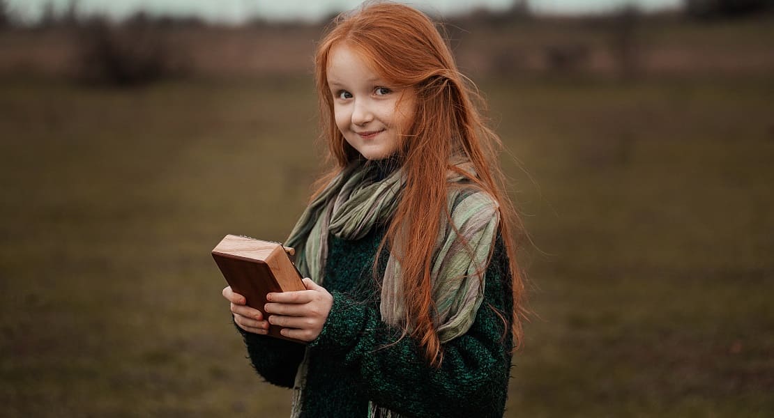 A redheaded little girl in a field playing a kalimba