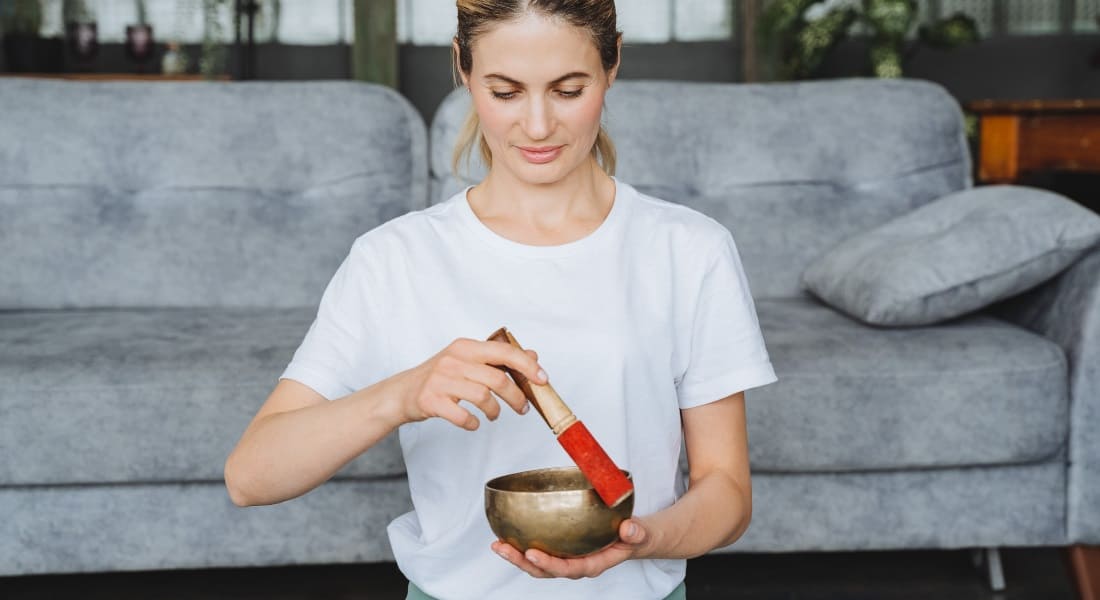 A seated woman meditating with a Tibetan singing bowl in her living room