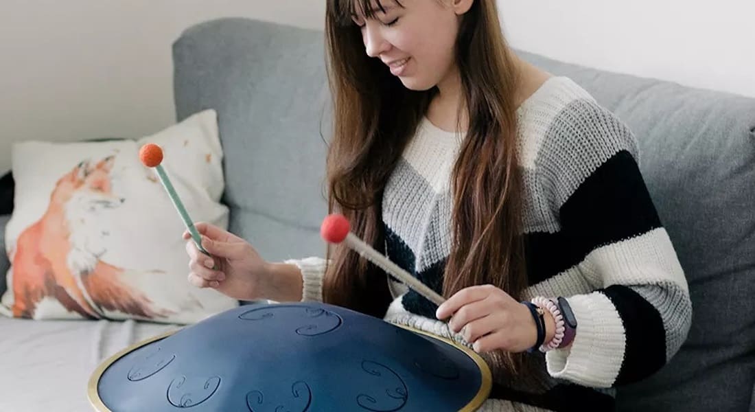 A woman on a couch playing a blue tongue drum