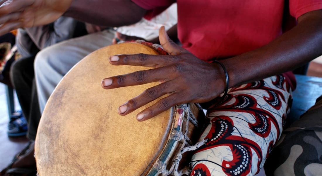 An African man wearing a red T-shirt with a djembe