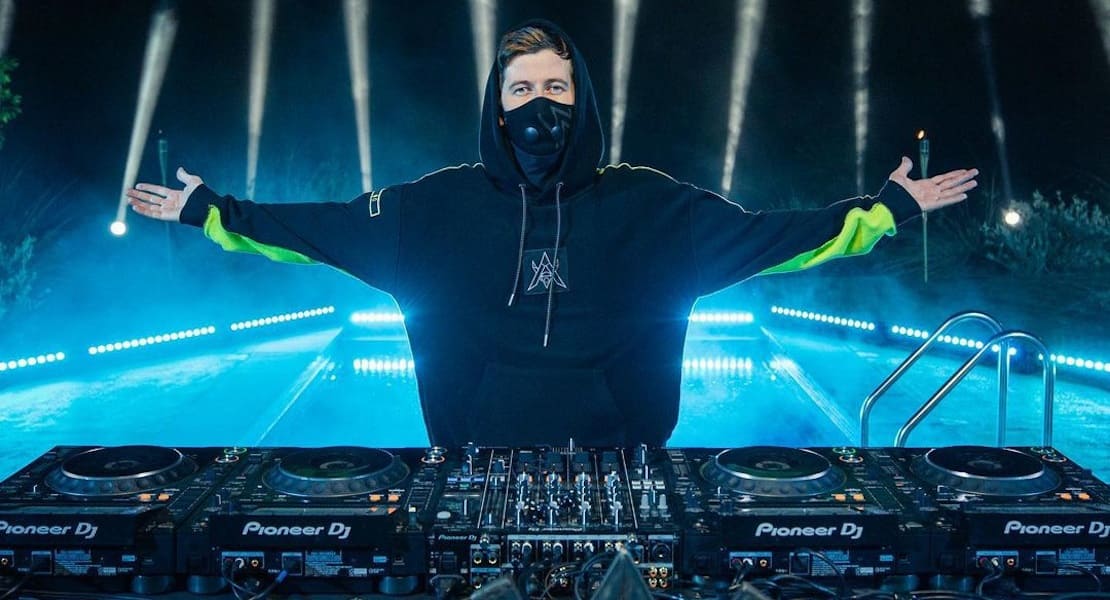 Alan Walker with arms outstretched behind the DJ decks