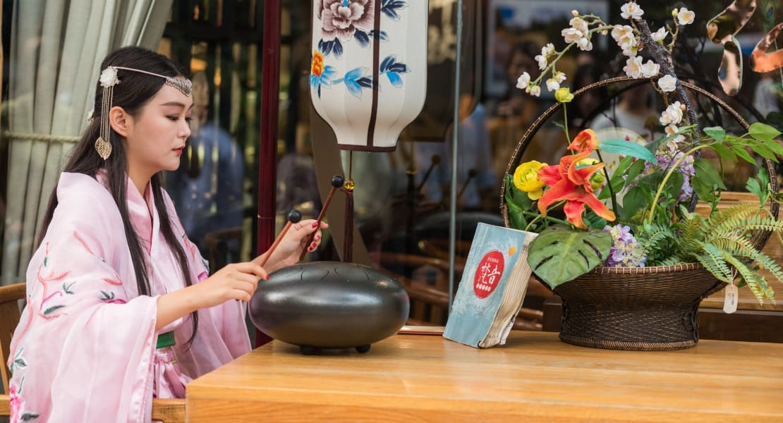 An Asian woman playing a tongue drum with mallets