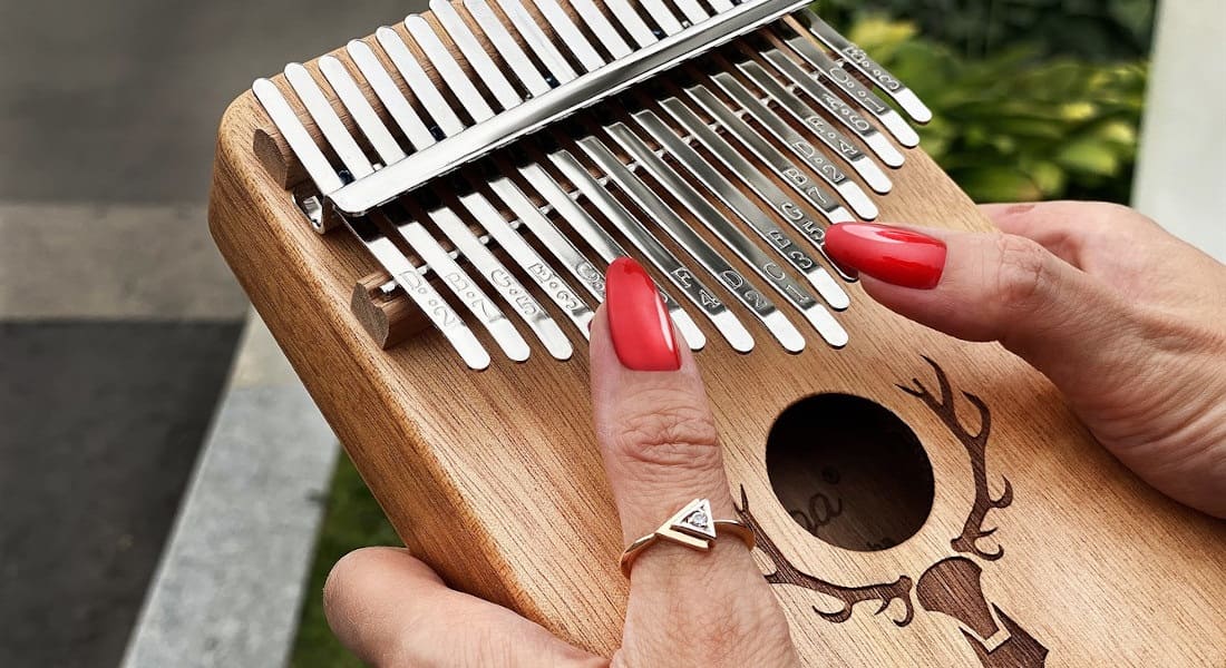 A close-up of two hands with red nails playing the kalimba