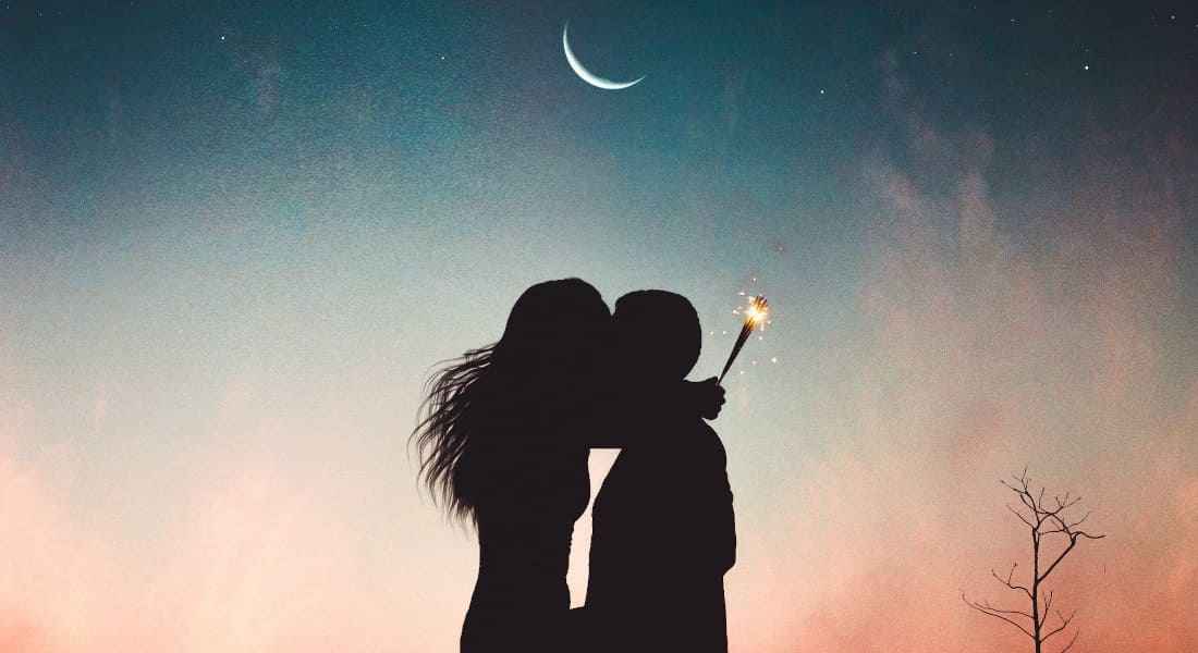 A couple kissing at night with a moon in the background