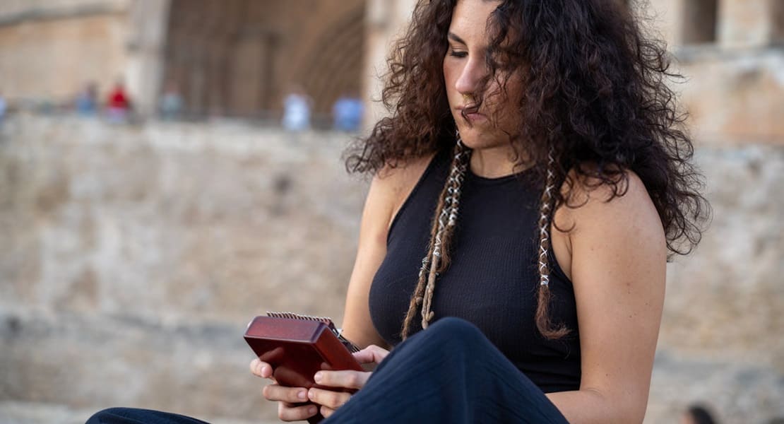 A woman with curly hair playing the kalimba while seated