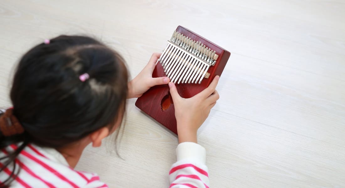 A girl seen from behind playing a kalimba while lying down