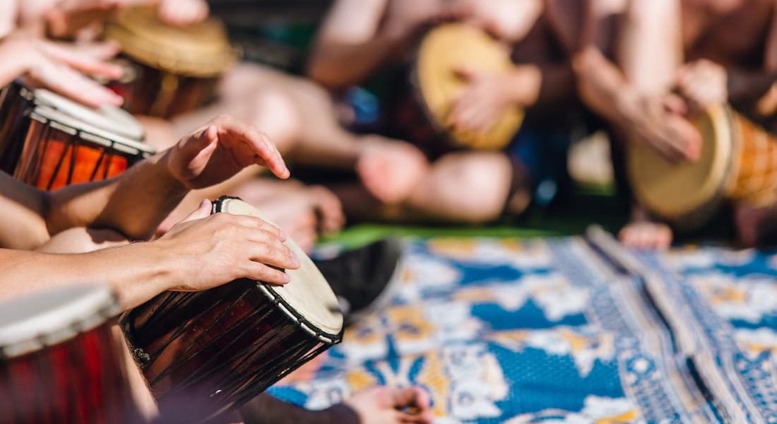 Several djembe musicians sitting together on a rug on the floor