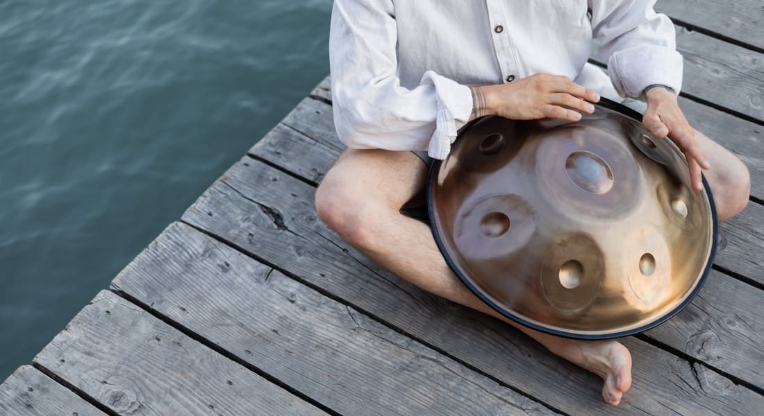 A handpan player sitting on a dock