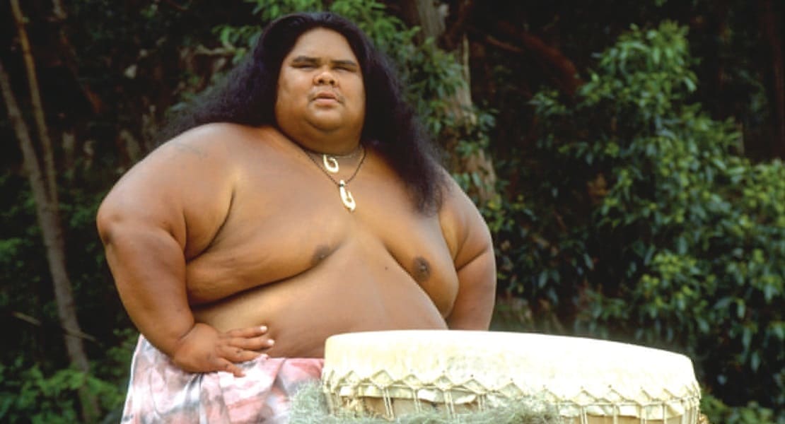 The singer IZ shirtless, standing in front of a drum