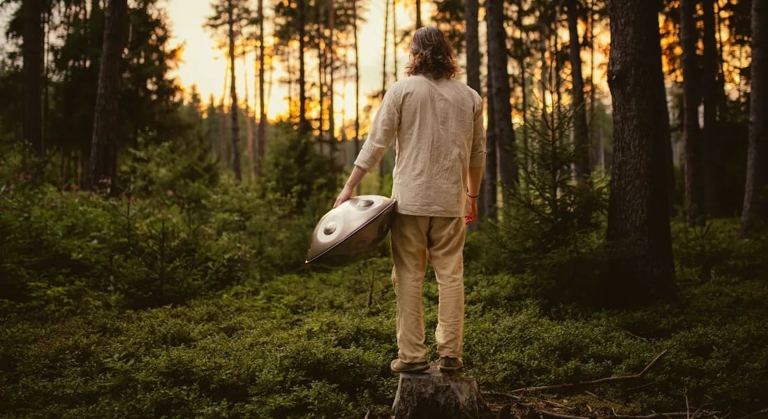 Konstantin Rössler seen from behind in a forest holding a handpan