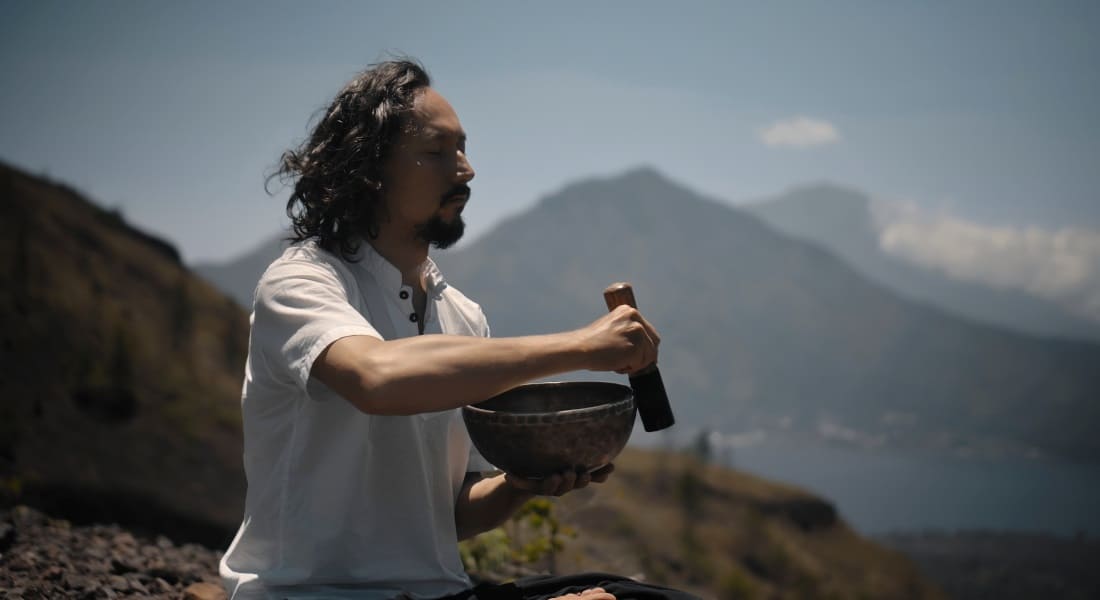 A man with his eyes closed playing a metal Tibetan singing bowl