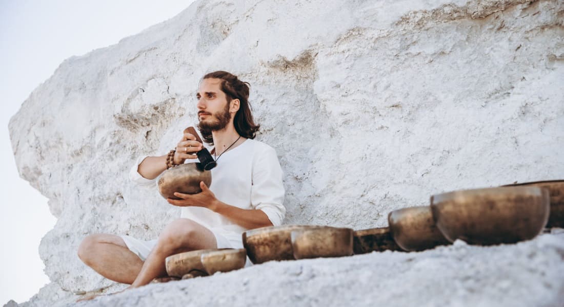 A man sitting in the mountains with about ten singing bowls around him
