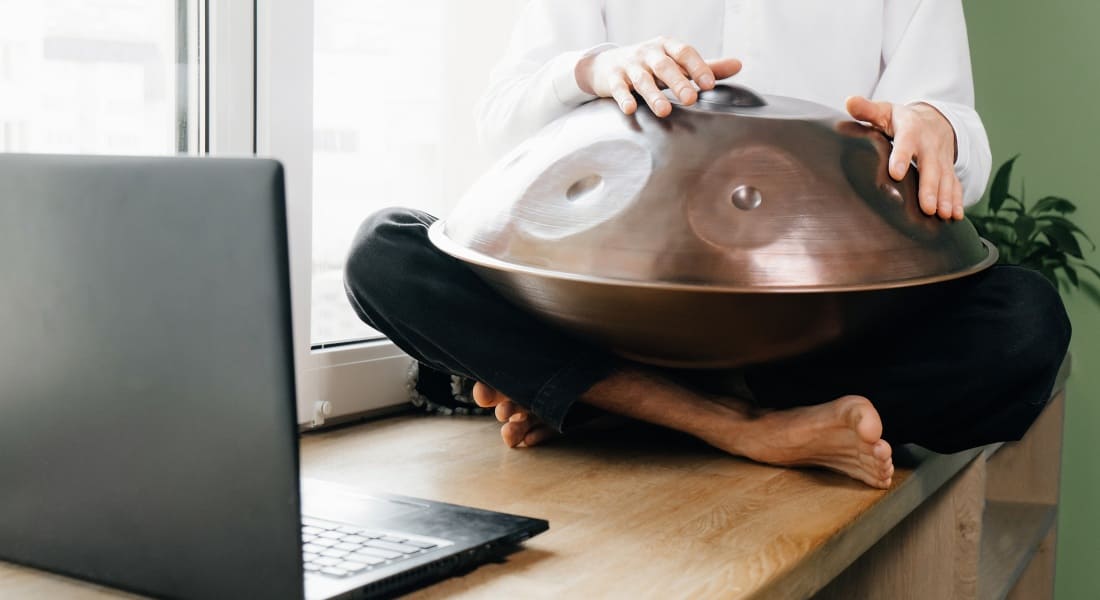 A man playing a handpan in front of a computer