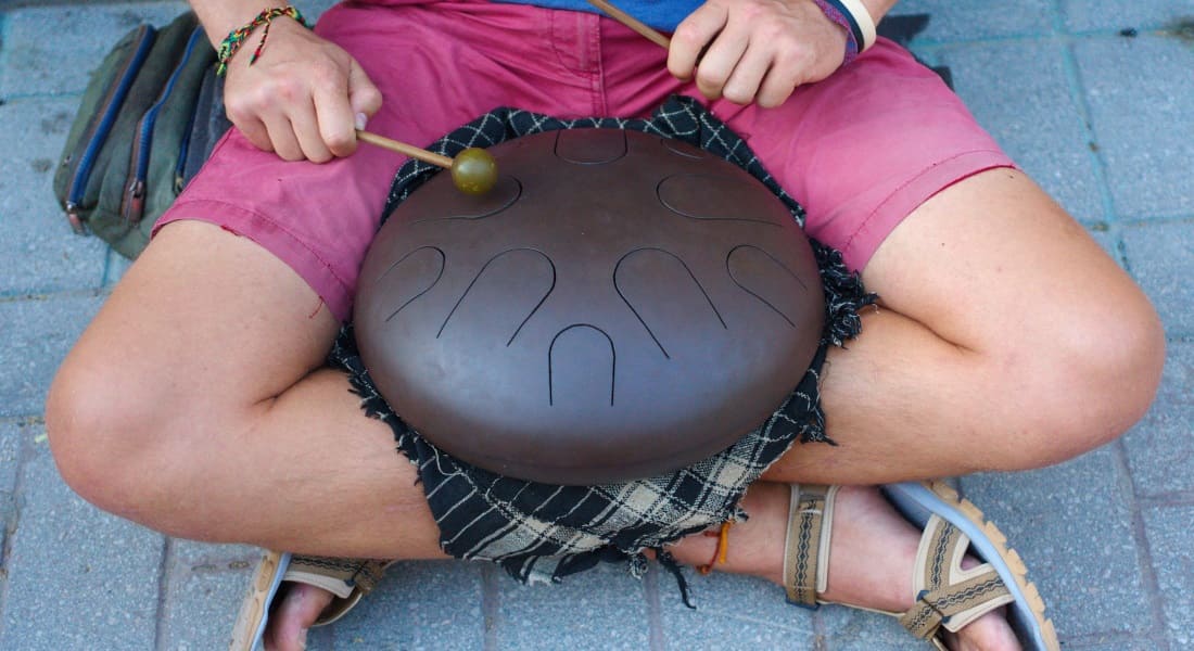 A man sitting cross-legged on the ground playing a tongue drum