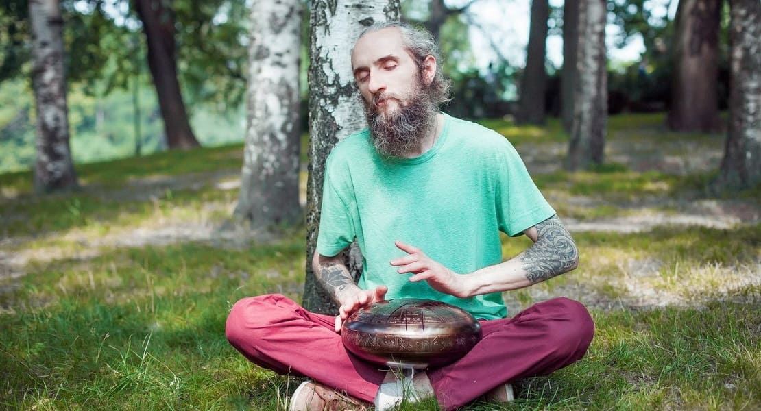 A man sitting in the grass playing a tongue drum
