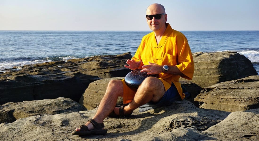 A man sitting on rocks at the beach with a tongue drum