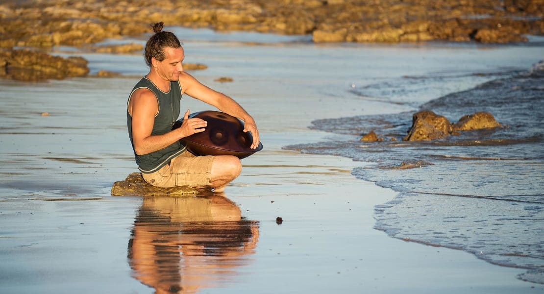 A man sitting in the sand playing a handpan