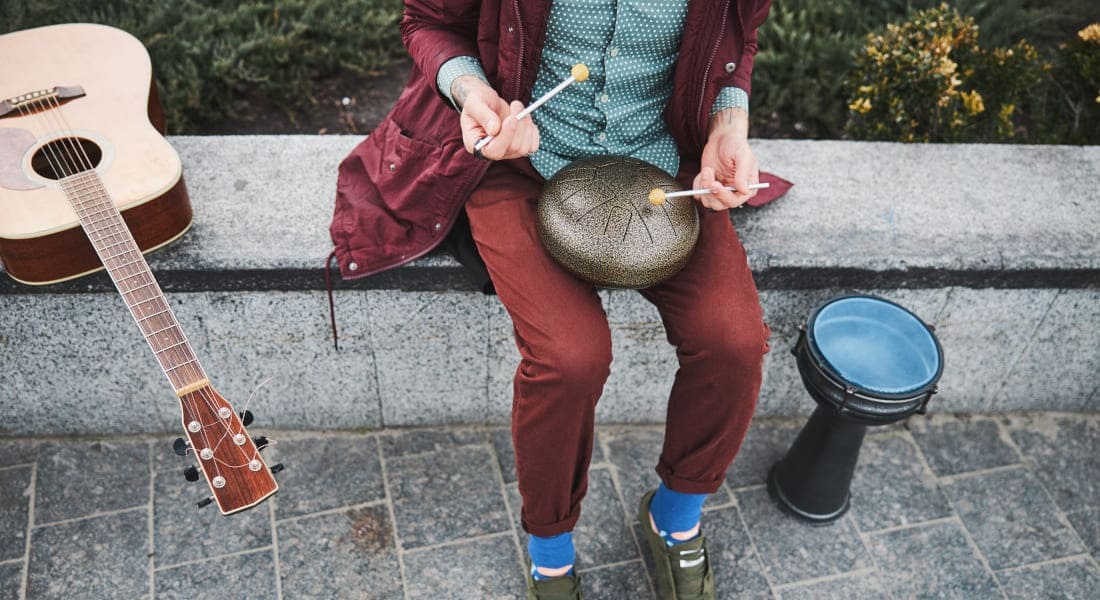 A man sitting in the street playing a tongue drum with mallets