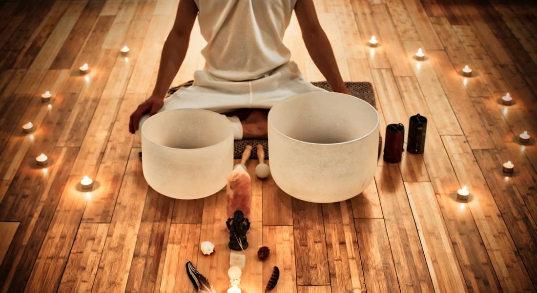 A person sitting cross-legged next to two crystal singing bowls
