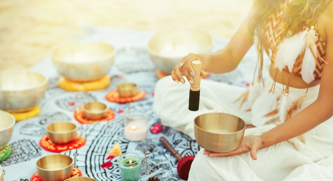 A seated woman surrounded by about twenty singing bowls
