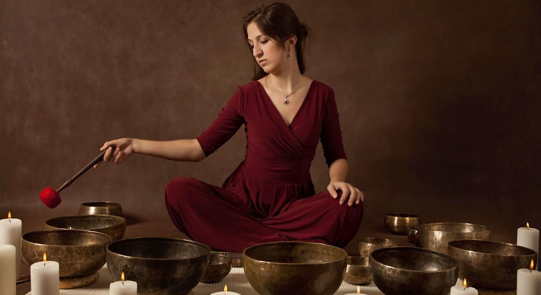 Seated woman using a mallet to play several Tibetan singing bowls