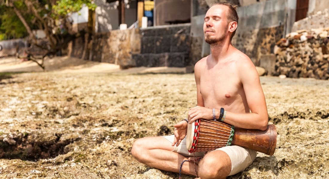 A shirtless man with his eyes closed holding a djembé