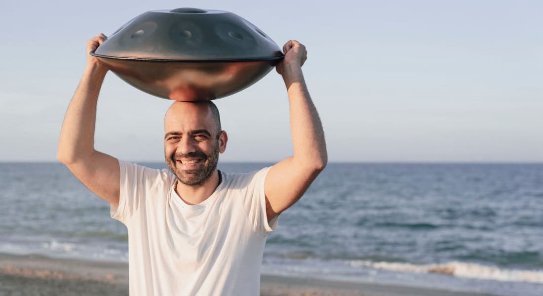 A smiling man with a handpan on his head