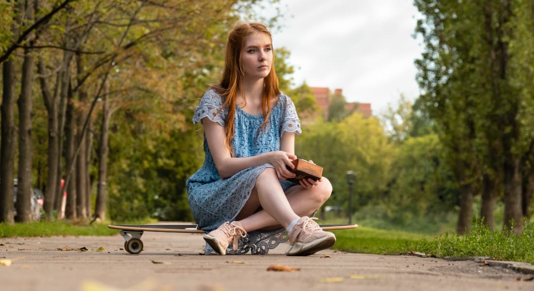 A thoughtful woman sitting on a skateboard holding a kalimba