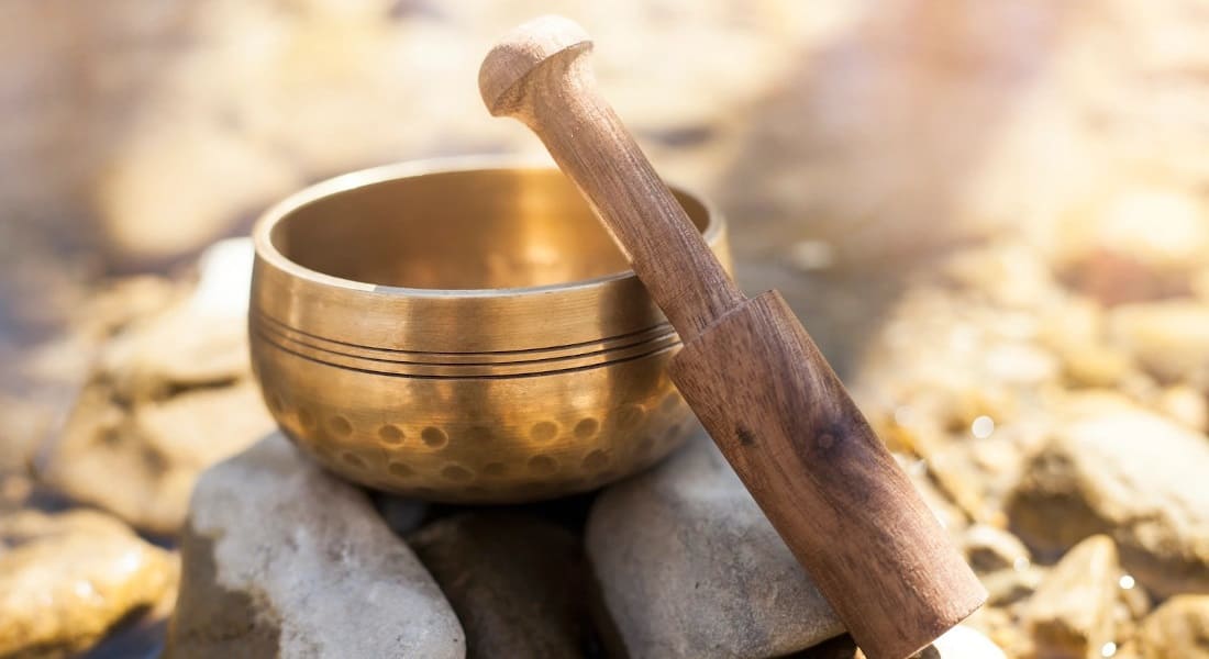 A Tibetan singing bowl on pebbles with a wooden mallet
