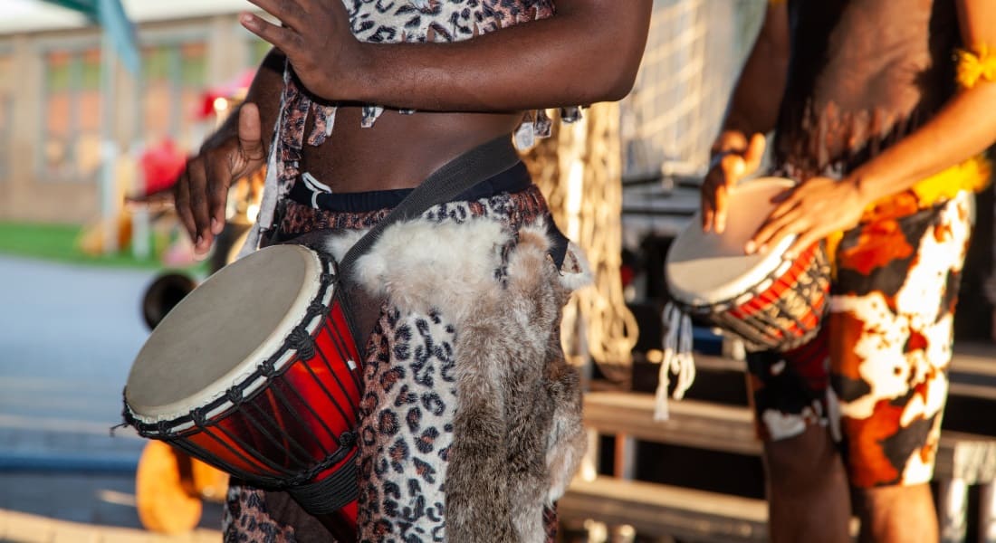 Two African men playing djembe with a harness