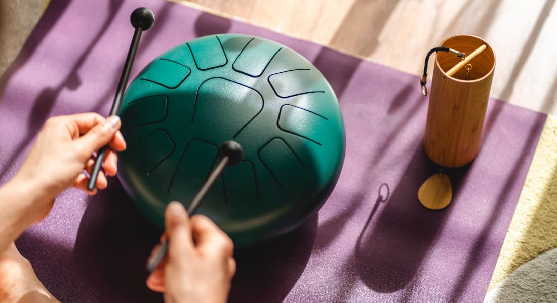 Two hands holding mallets to play a green tongue drum