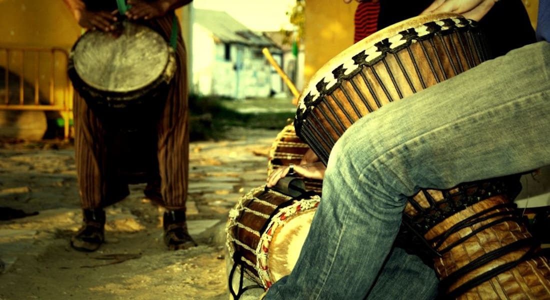 Two musicians playing a djembe between their legs
