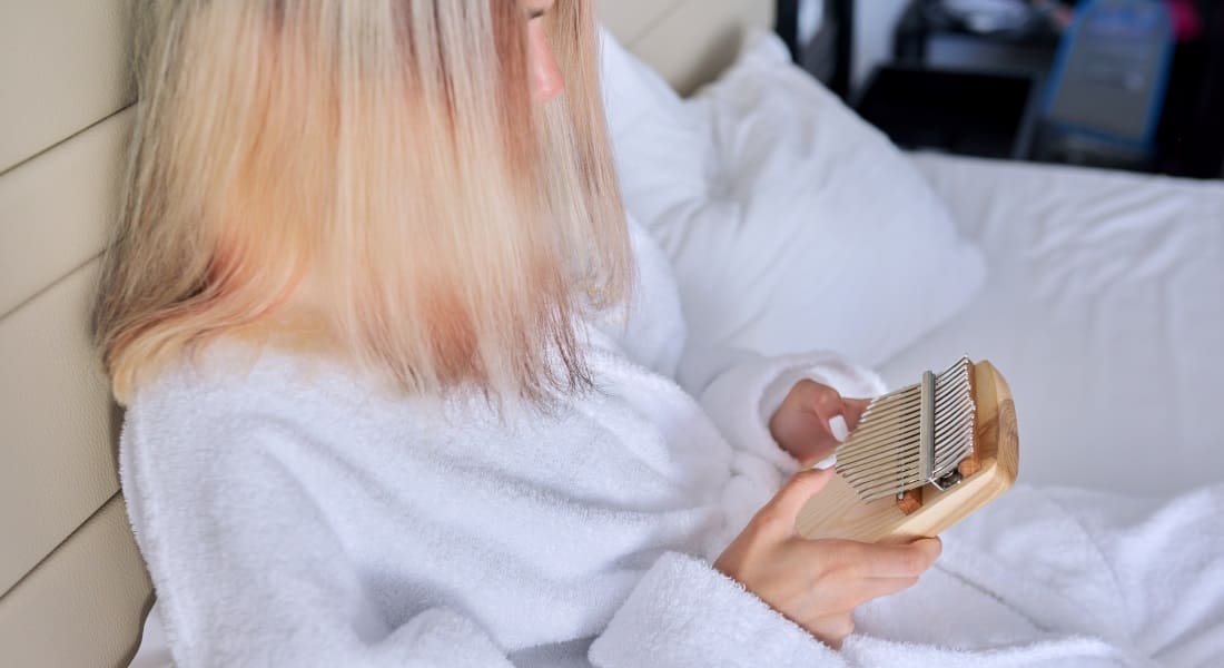 A woman in a bathrobe in bed playing a kalimba
