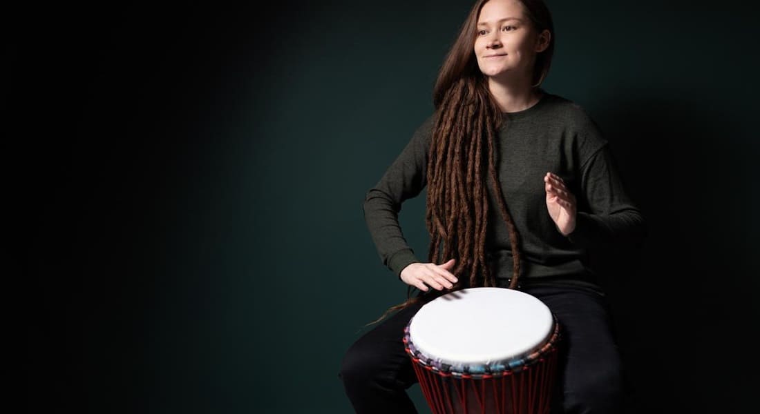 A woman playing djembe against a black and green background