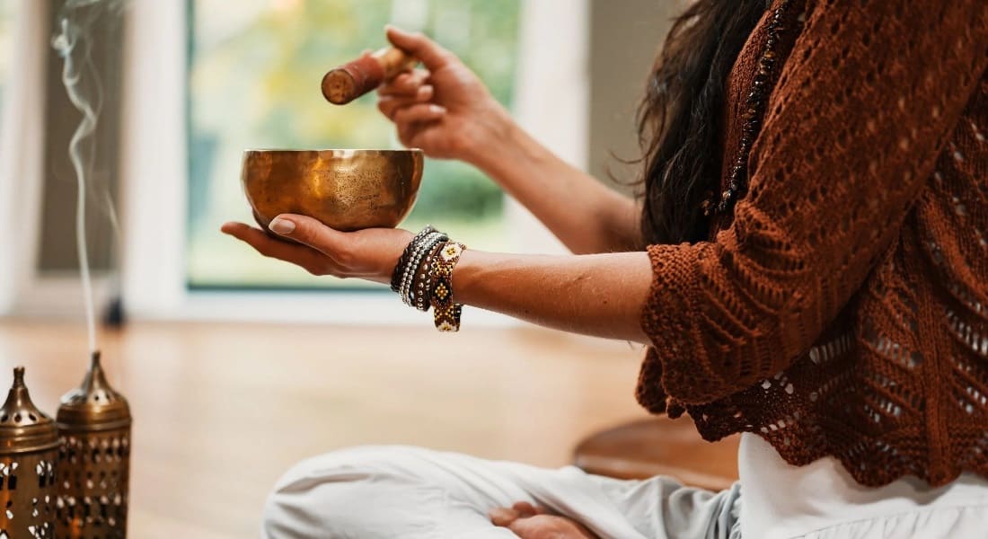 A woman cleansing a room with a singing bowl and incense