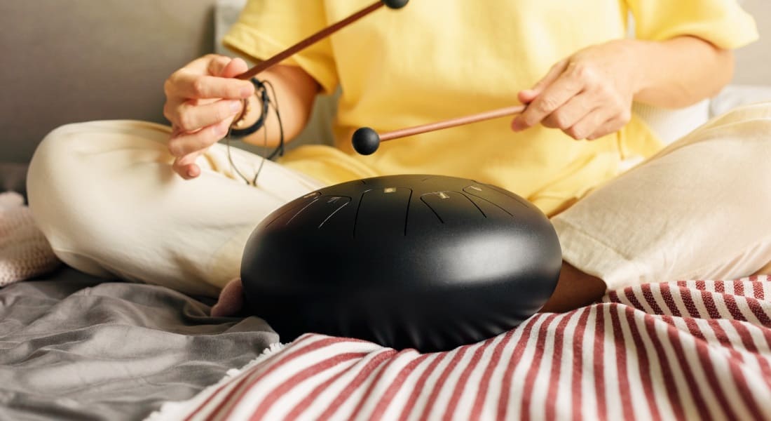 A woman sitting cross-legged on a bed playing a tongue drum