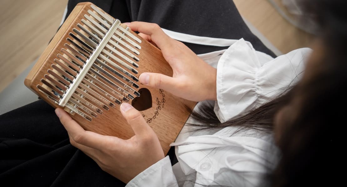 A woman sitting cross-legged playing the kalimba with a heart