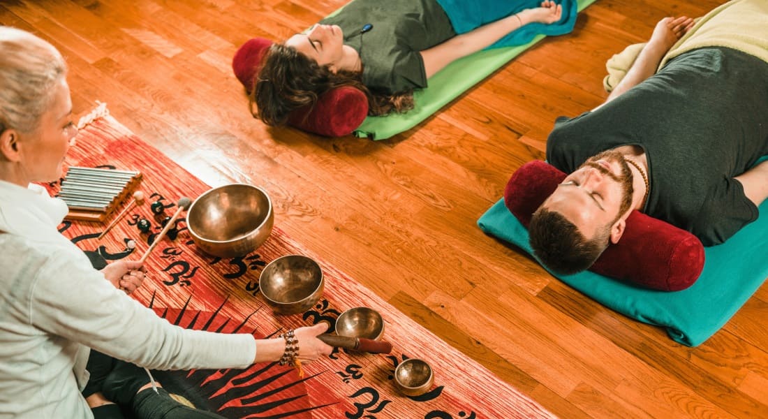 A woman leading a group sound massage with Tibetan singing bowls