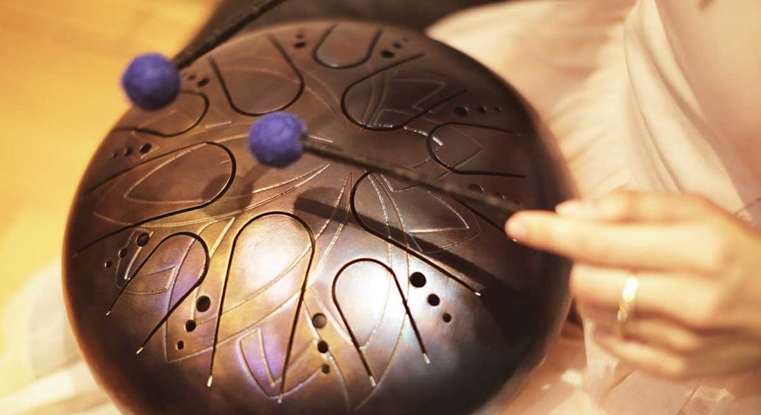 Two women's hands holding mallets while playing a tongue drum