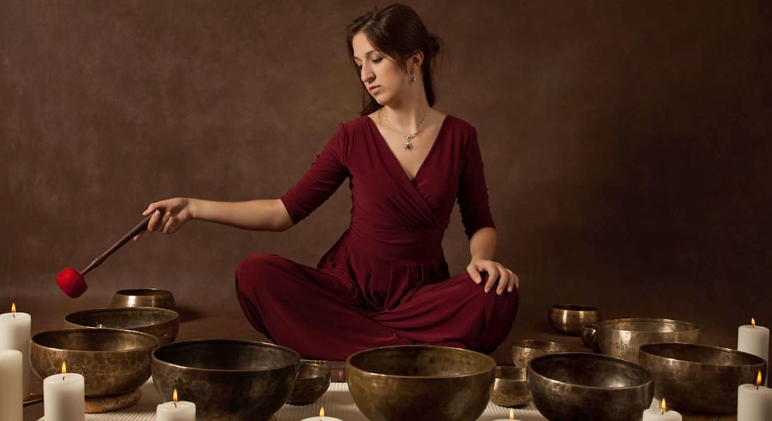A woman in a red dress surrounded by singing bowls