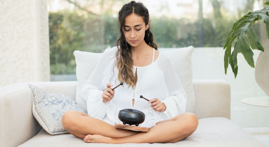A woman sitting in lotus pose playing a zen drum