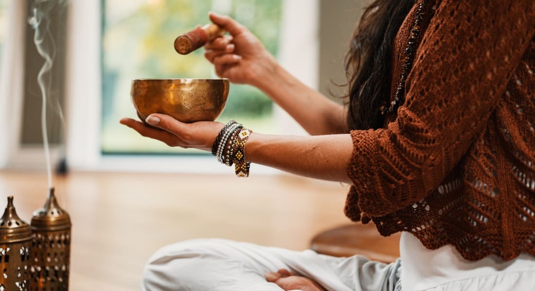 A woman playing a Tibetan singing bowl surrounded by incense