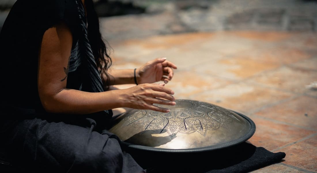 A woman playing a tongue drum while sitting on the floor