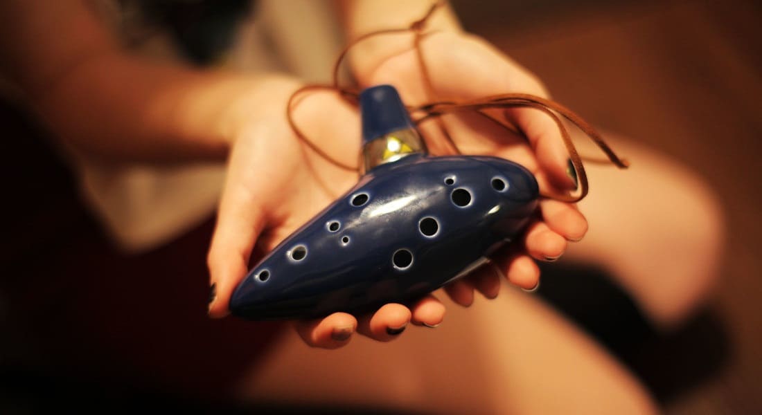 A woman presenting a blue ocarina in the palm of her hands