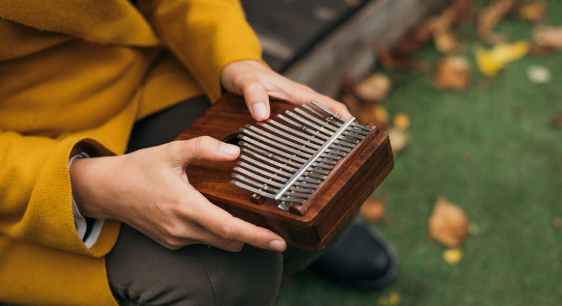 A woman sitting in a yellow coat playing the kalimba