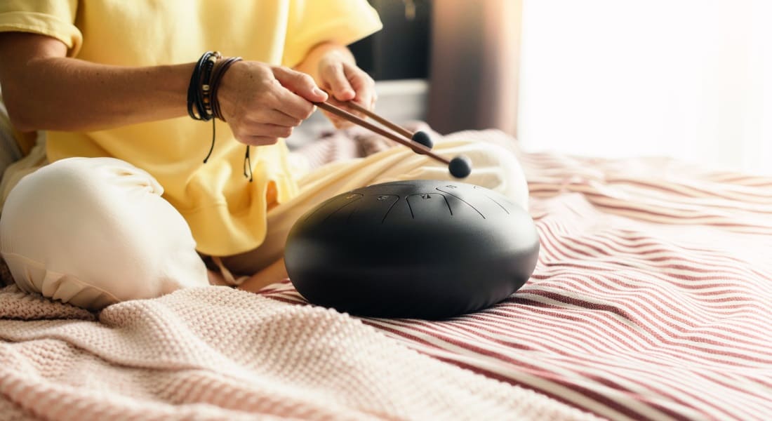A woman sitting cross-legged on a bed with a tongue drum