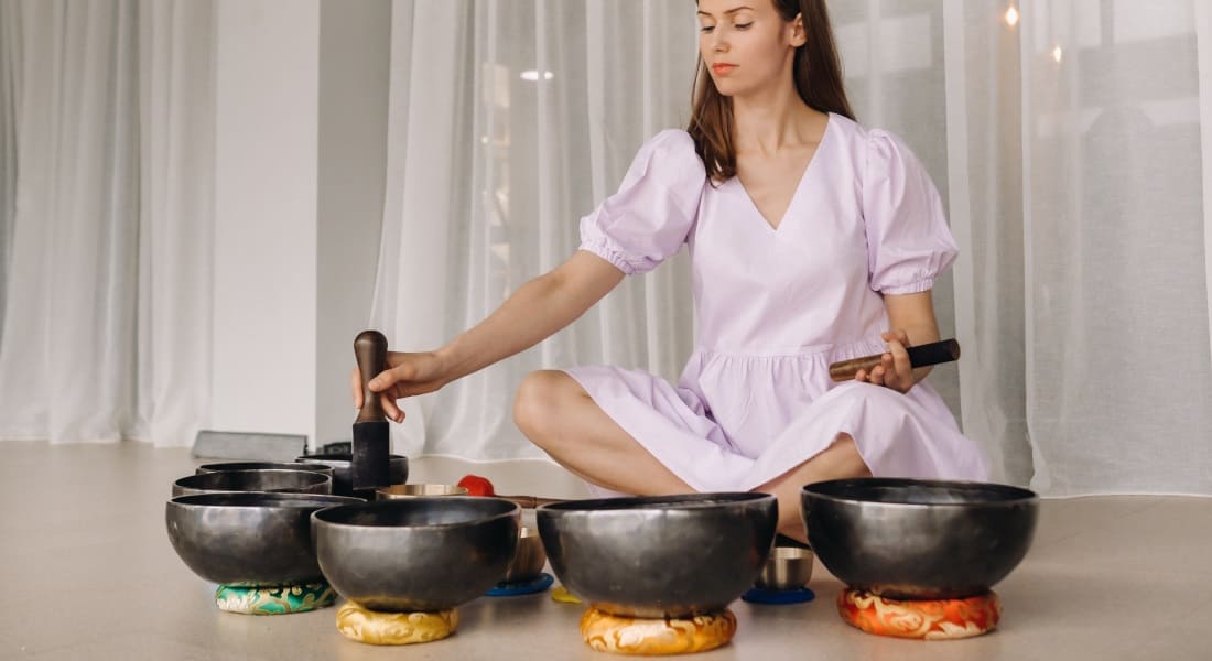 A woman sitting on the floor with about ten Tibetan bowls in front of her